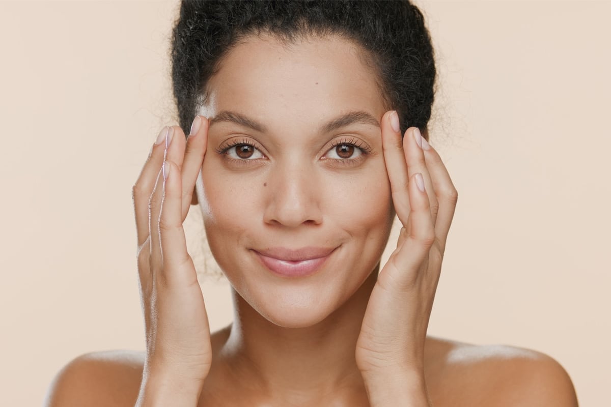 Woman gently touching her temples, exploring non-surgical eye rejuvenation.