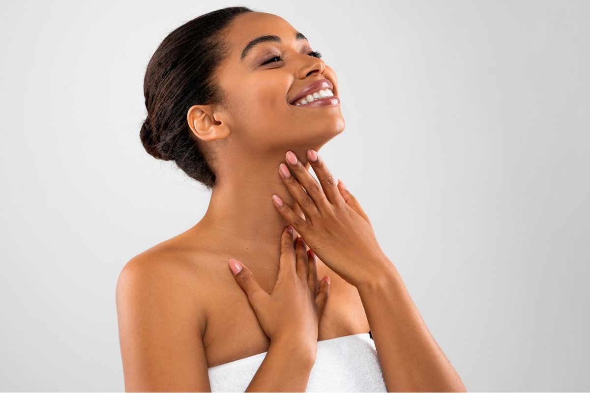 Woman with a radiant smile touching her defined jawline, symbolizing Kybella's effect.