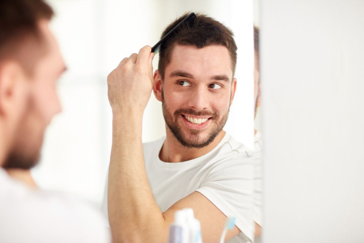 Smiling man combing his hair, enjoying the results of PRP hair restoration therapy.